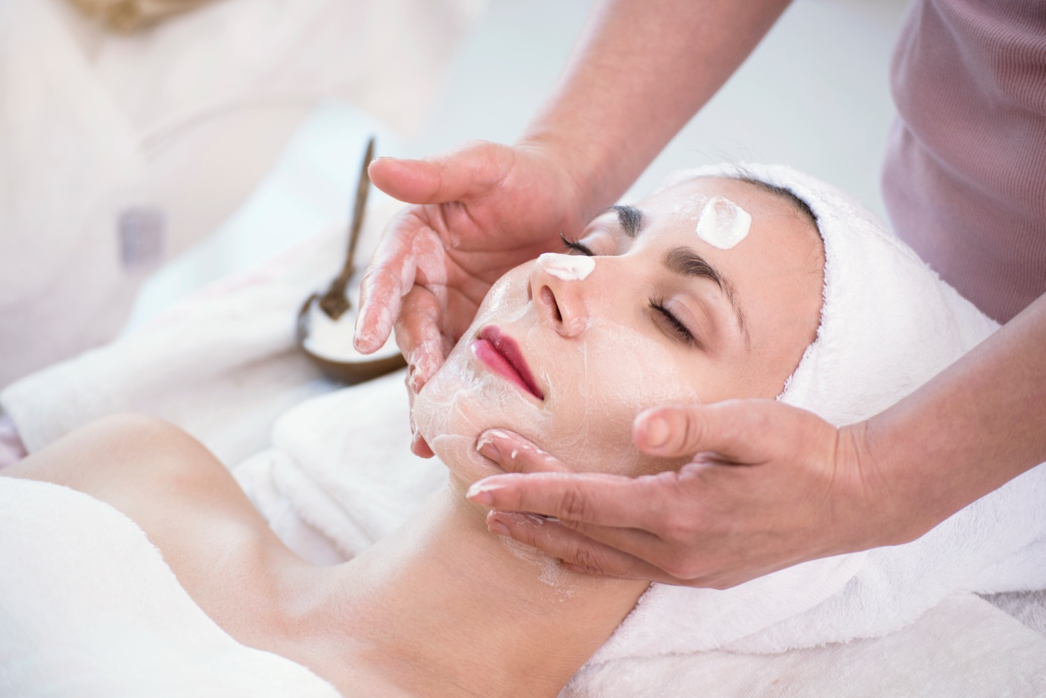 A client receiving a cream-mask facial while a therapist smooths product across the cheeks.